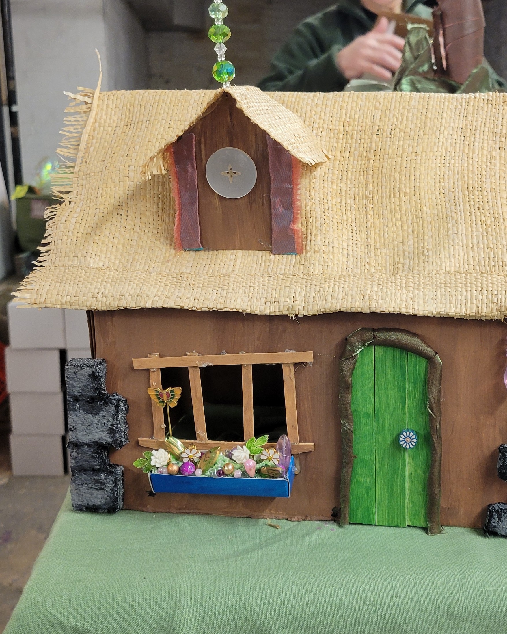 Diorama of a cottage with a straw roof, a window with flower box, and a green door.