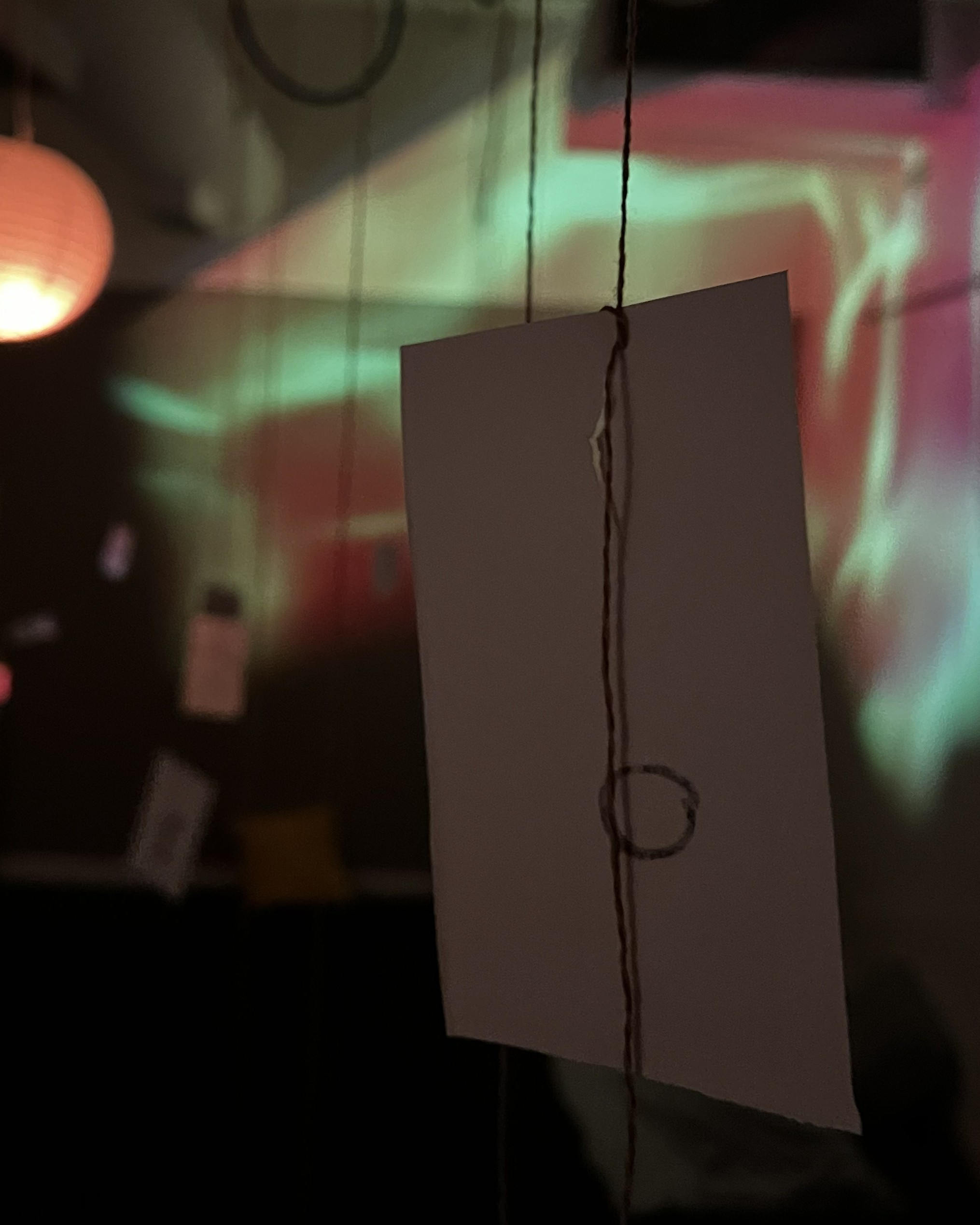 A close-up picture of an index card hanging from a string, with muted warm colors and light projected in the background.
